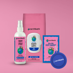 Collection of Earthbath pet care products including a spray, wipes, shampoo, and a bag on a pink background.