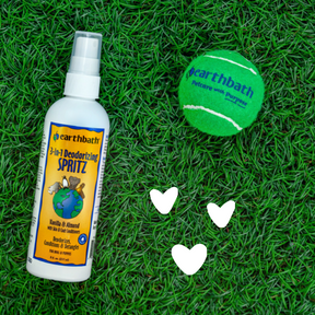 earthbath 3-in-1 Deodorizing Spritz bottle and green tennis ball on grass with hearts around